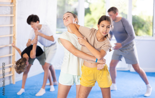 Two preteen girls train in pairs at self-defense lesson under guidance of trainer in the gym