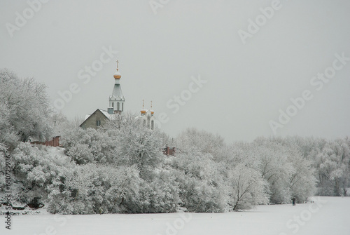 Winter landscape on a frozen lake. White snow on the trees and a church on the shore.