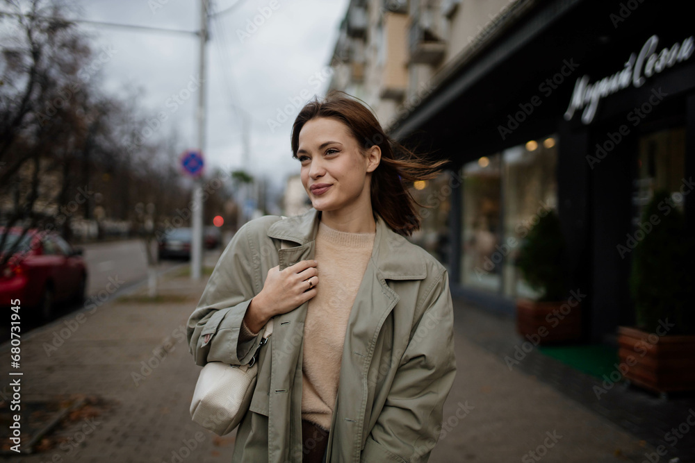 Fototapeta premium cute young woman in a green coat and sweater walks around the city and smiles