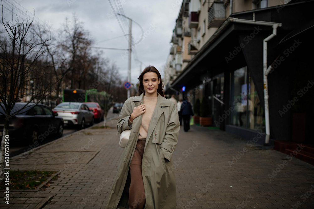 cute young woman in a green coat and sweater walks around the city and smiles