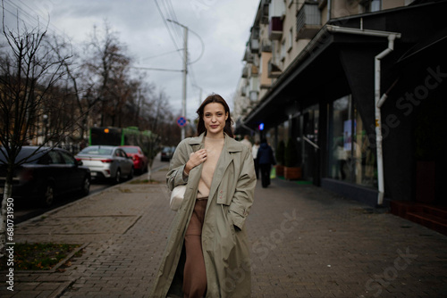 cute young woman in a green coat and sweater walks around the city and smiles © velimir