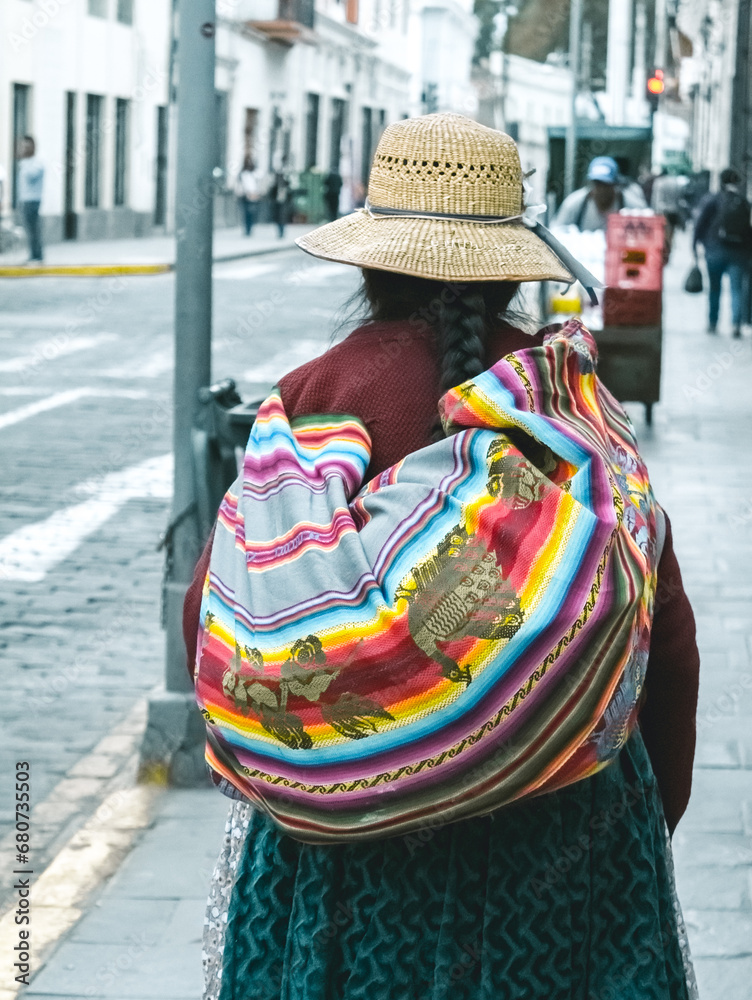 Peruvian woman walking in the street in Arequipa, Peru, and wearing traditional clothes. She also wears a typical colorful bag in her back and a straw hat.