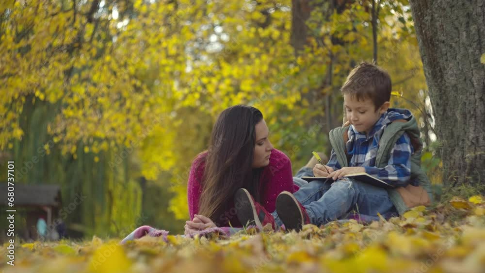 Harmonizing Homework and Happiness: Mom's Supportive Presence Enhances the Tranquility of the Autumn Park. High quality 4k footage Harmonizing Homework and Happiness: Mom's Supportive Presence Enhances the Tranquility of the Autumn Park. High quality 4k footage