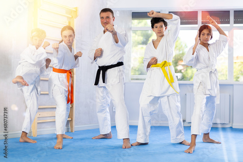 Group of children in kimonos and karateka trainer pose while standing in studio