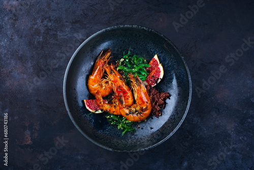 Traditional fried king prawns with fig pieces, brown rice and wakame served as top view on a design bowl with text space