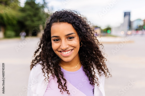 Happy young latin american girl smiling at camera standing at city street. Outside portrait of joyful beautiful woman over urban background.