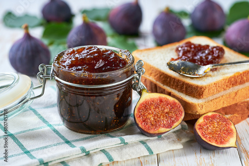 Homemade jam. A glass jar of figs jam on a white wooden table. Homemade figs marmalade and fresh figs and green leafs on the kitchen table.