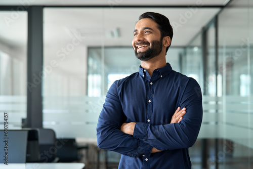 Happy confident Indian business man leader looking away standing in office. Smiling professional businessman manager executive, male worker from India feeling cheerful thinking of financial success. photo