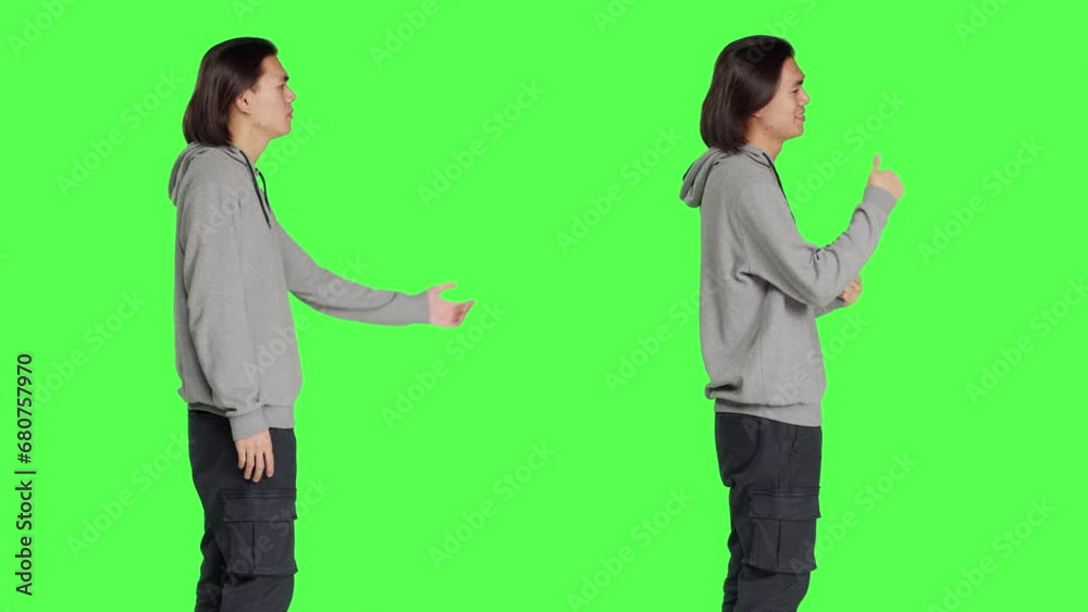 Asian adult does thumbs up symbol standing against greenscreen backdrop, showing approval and presenting like gesture on camera. Young positive person feeling pleased, agreement. Asian adult does thumbs up symbol standing against greenscreen backdrop, showing approval and presenting like gesture on camera. Young positive person feeling pleased, agreement.