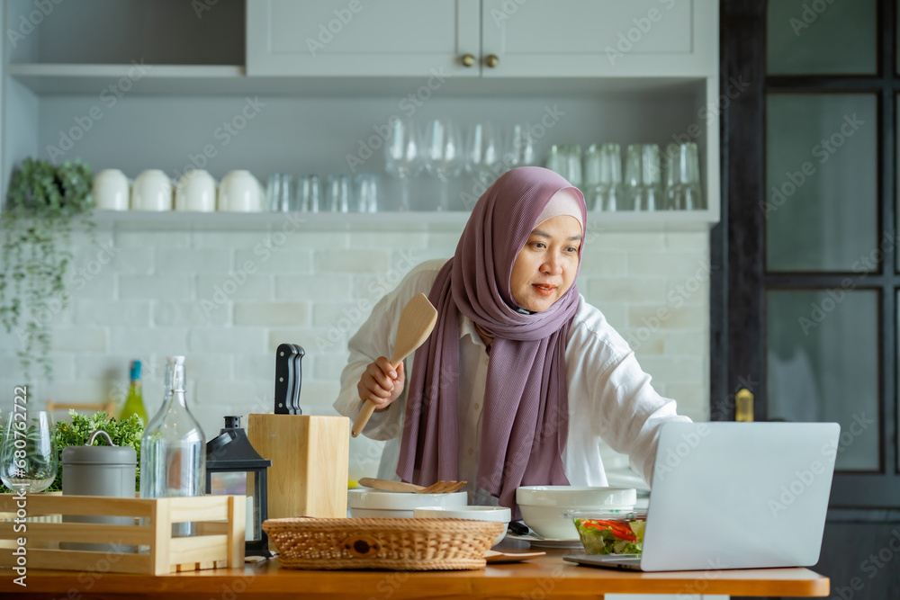 muslim mother looking at recipe from laptop and cooking. having fun woman with hijab preparing dinner, Islamic woman Enjoying Doing Homemade, Teaching cooking online muslim mother looking at recipe from laptop and cooking. having fun woman with hijab preparing dinner, Islamic woman Enjoying Doing Homemade, Teaching cooking online