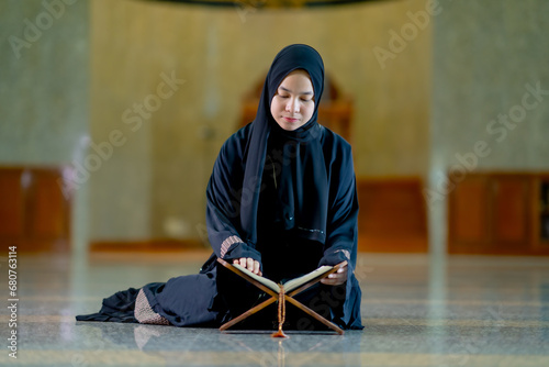 The image of an Asian Muslim woman in the Islamic religion in hijab in black color. reading the Quran and having a happy Staying in a beautiful mosque, Arabic word translation: The Holy Al Quran.