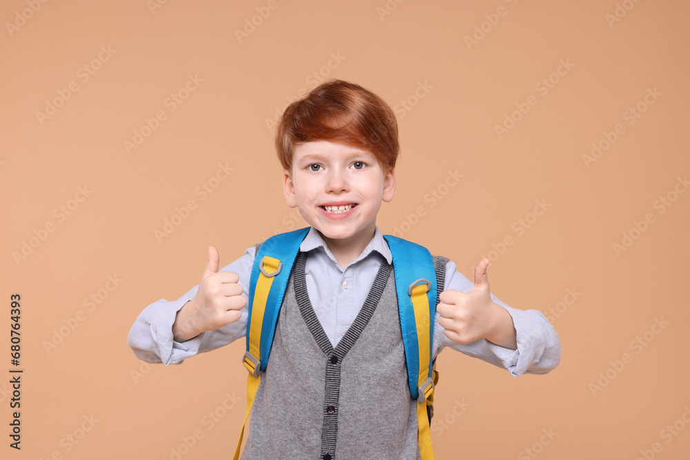 Smiling schoolboy showing thumbs up on beige background Smiling schoolboy showing thumbs up on beige background