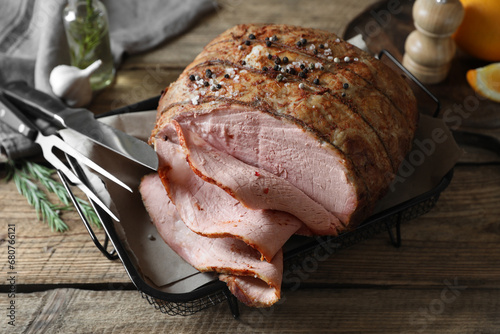 Delicious baked ham, carving fork, knife and rosemary on wooden table