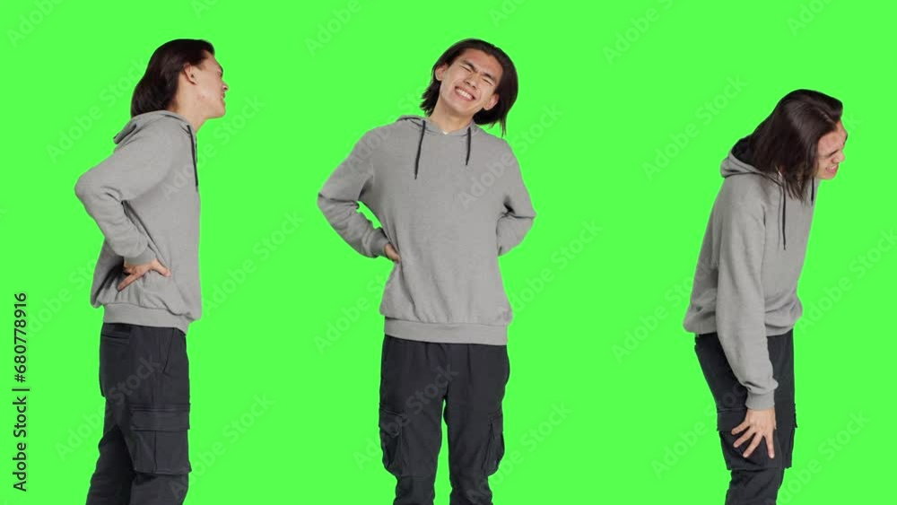 Male model suffering from back pain in studio, dealing with lower spine cramps while he is standing over greenscreen. Young adult being in pain and suffering from spinal pressure, backache. Male model suffering from back pain in studio, dealing with lower spine cramps while he is standing over greenscreen. Young adult being in pain and suffering from spinal pressure, backache.