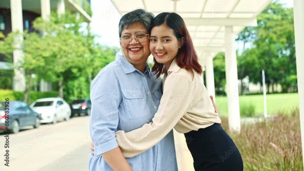 Family portrait happy elderly mother and her cute beautiful healthy asian daughter stand in an embrace smiling and good mood looking at the camera while standing in an outdoor park. Family portrait happy elderly mother and her cute beautiful healthy asian daughter stand in an embrace smiling and good mood looking at the camera while standing in an outdoor park.