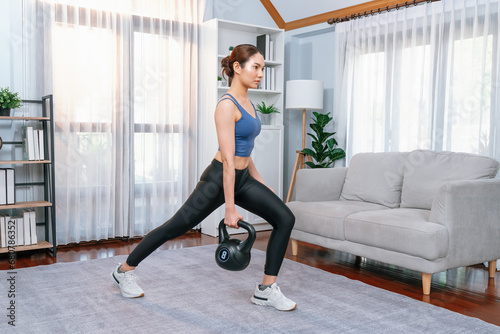Vigorous energetic woman doing kettlebell weight lifting exercise at home. Young athletic asian woman strength and endurance training session as home workout routine. photo