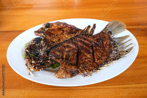 Gurame Bakar Madu, Grilled Gourami with honey and soy sauce. Served with sambal (chilli sauce), cucumber and tomatoes in white plate.   
