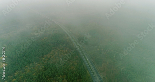 Drone road. Misty countryside. Nature scenery. Trees crowns and long asphalted way in fog on autumn cloudy dull day aerial view.