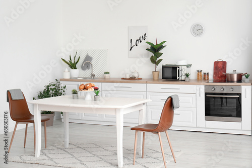 Interior of modern kitchen with pastry and houseplants on dining table