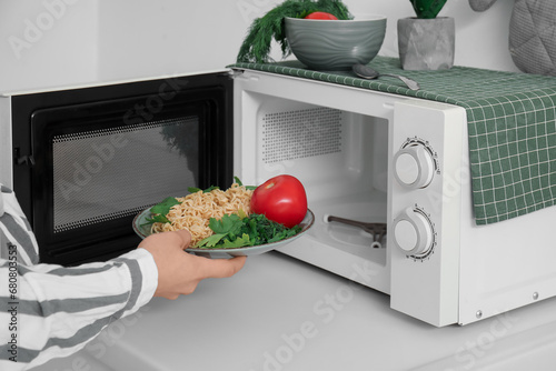 Woman putting plate with pasta into microwave oven in modern kitchen