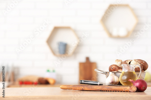 Colander with fresh mushrooms and cooking utensils on table in kitchen