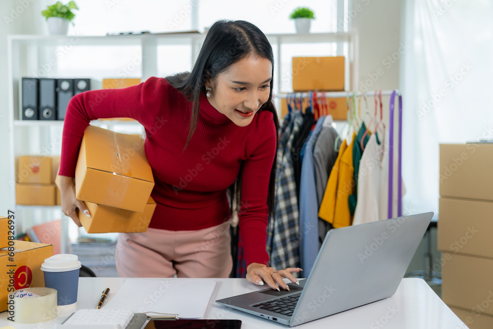 Asian female entrepreneur SME business owner works with laptop, box and phone to shop online at home. Online Marketing SME Ecommerce Online Packaging Delivery