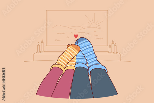 Feet of loving couple in autumn warm socks lying on sofa and watching TV in romantic home atmosphere. Couple spending time together and enjoying comfort during autumn weekend or vacation