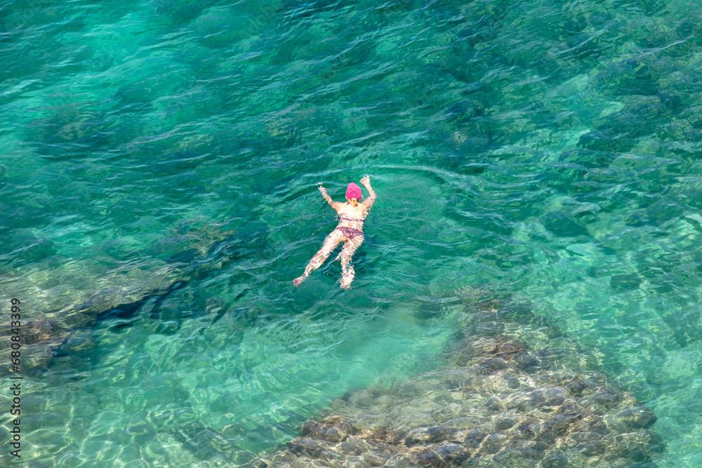 Woman swim in open sea in turquoise water. View from above