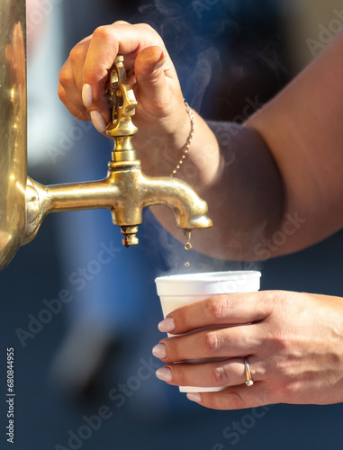 A woman pours tea into a glass from a samovar