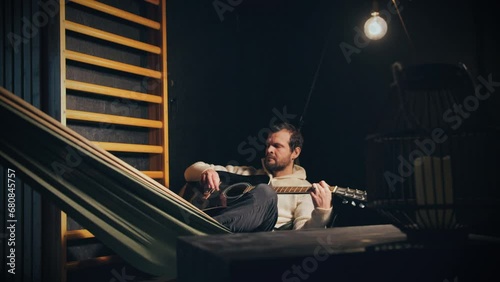 Musician playing his guitar unpretentiously lying on hammock at home. Static photo