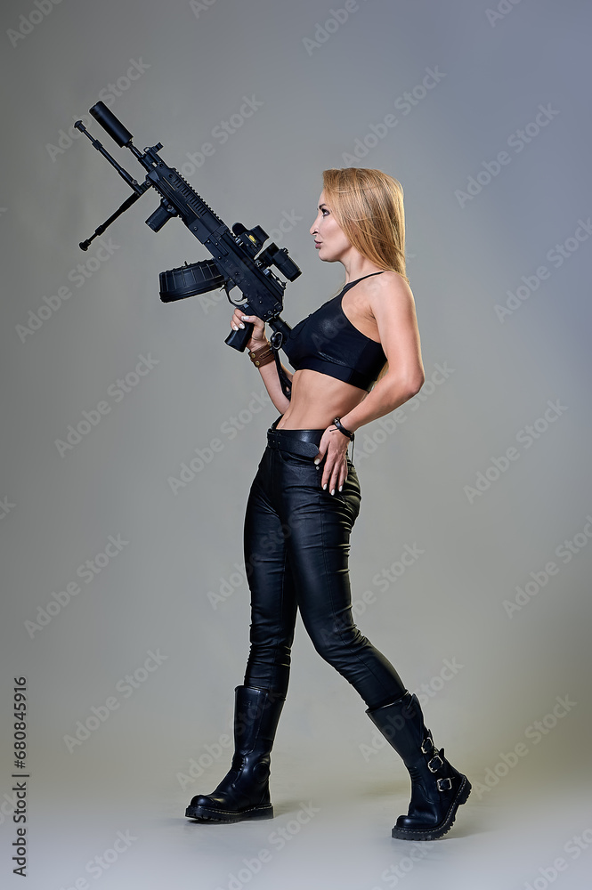 slender beautiful woman in a black leather suit with a machine gun in her hands on a gray background slender beautiful woman in a black leather suit with a machine gun in her hands on a gray background