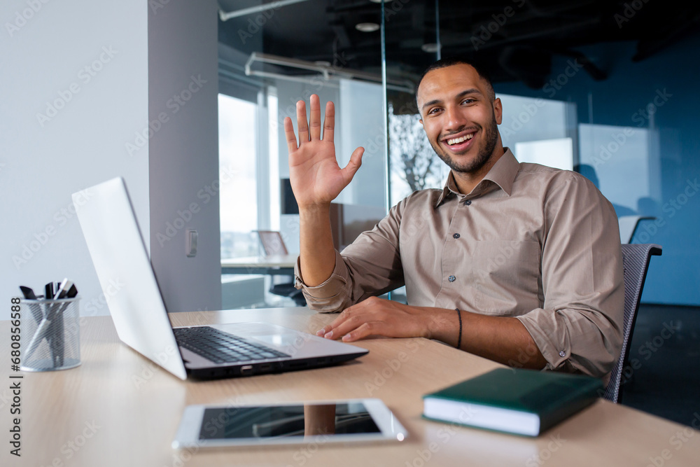 Portrait Satisfied African American businessman in office, working on laptop, tapping on keyboard, greeting waving hand looking at camera. Portrait Satisfied African American businessman in office, working on laptop, tapping on keyboard, greeting waving hand looking at camera.