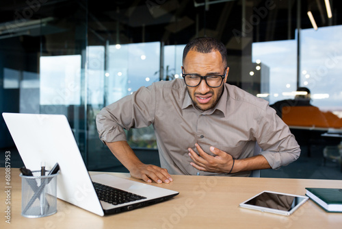 Man in the office holding his hand on his chest, heart attack at the workplace, health problems due to work in the office.