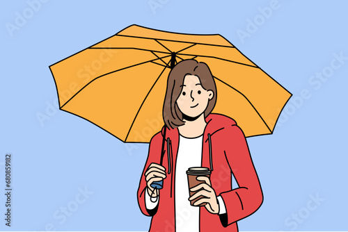 Woman holds plastic cup with coffee takeouts and umbrella protecting from rain during autumn walk. Girl enjoys taste of invigorating takeouts coffee and looks at screen with thoughtful grin.