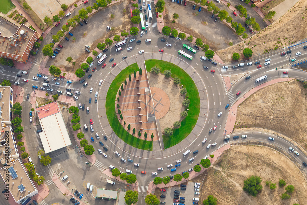 Aerial view of car traffic at circle roundabout intersection with fast moving heavy traffic. Urban circular transportation crossroads at day. High Up Traffic Timelapse. Directly above a roundabout. 