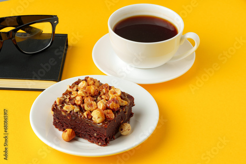 Piece of brownie cake with hazelnuts on yellow background