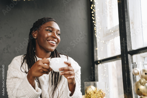 African woman in warm white sweater drinking hot coffee or tea at home photo