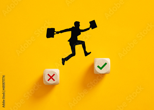 Silhouette of a businessman jumping from wrong cross symbol to right check mark symbol on wooden cubes. photo