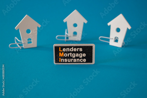 Wooden houses sits next to a wooden black board with the word lenders mortgage insurance. Beautiful blue background. Business and LMI  lenders mortgage insurance concept.