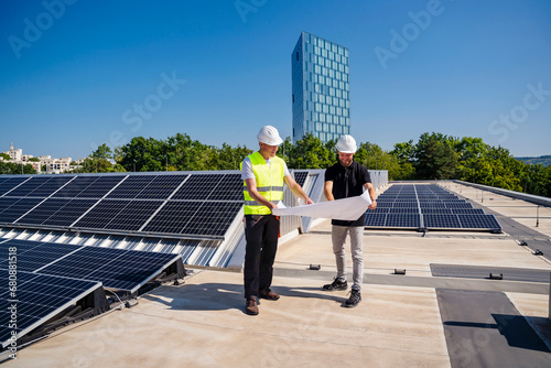 Two technicians strategizing on the rooftop of a corporate building equipped with solar panels photo