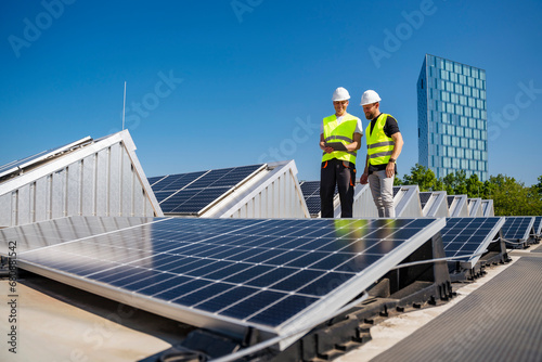 Two technicians utilizing a tablet PC while working on the rooftop of a corporate building equipped with solar panels photo