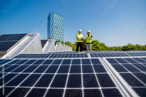 Two technicians utilizing a tablet PC while inspecting solar panels on the rooftop of a corporate building photo