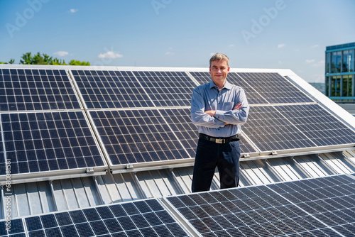 A self-assured businessman stands proudly surrounded by rows of gleaming solar panels