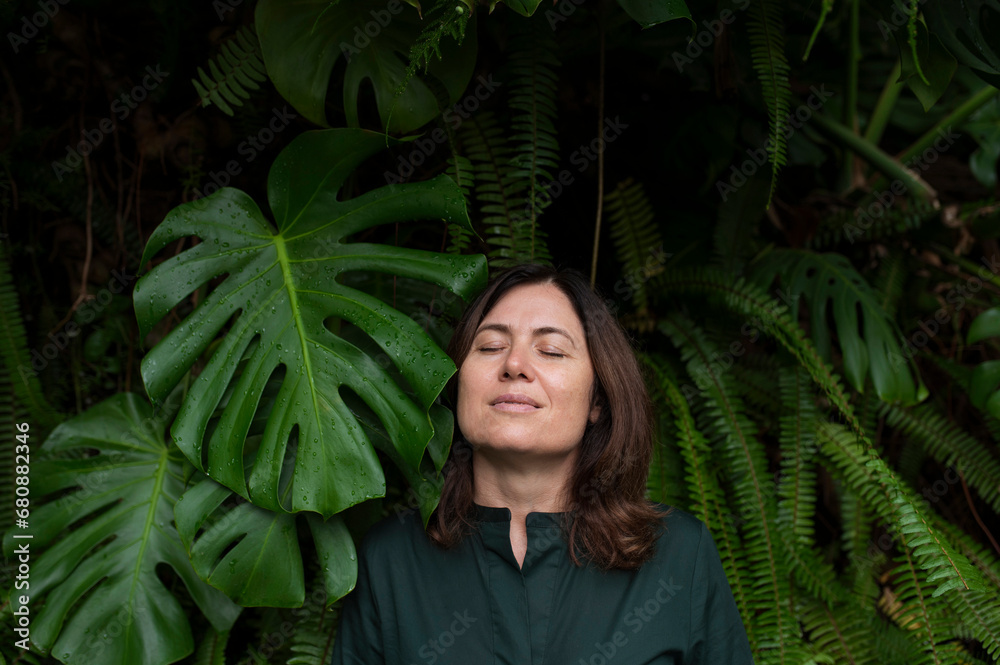 Happy woman with eyes closed amidst leaves in botanical garden