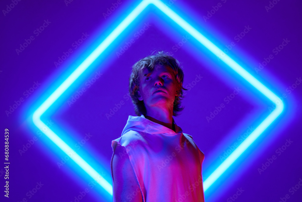 Futuristic portrait of handsome, calm man posing in neon light against background with abstract digital, projector reflection.