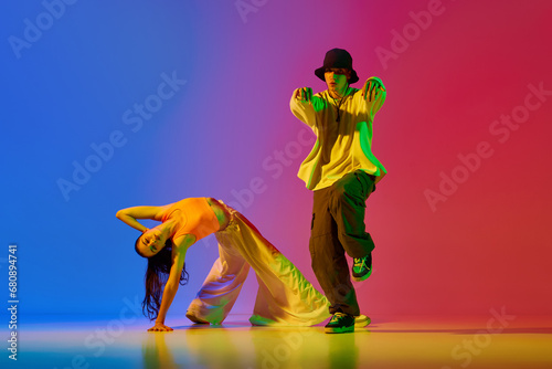 Fototapeta Naklejka Na Ścianę i Meble -  Stylish, young, active and talented boy and girl in modern clothes dancing hip-hop against blue red background in neon light. Concept of hobby, action, street style, contemporary dance, youth, fashion