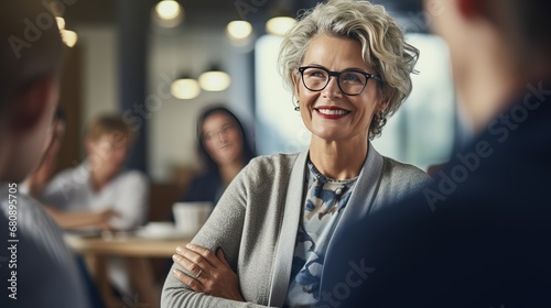 Smiling aged businesswoman in glasses looking at colleague at team meeting, happy attentive female team leader listening to new project idea, coach mentor teacher excited by interesting discussion.