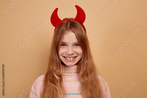 Little girl with red devil horns happy and smiling expression.