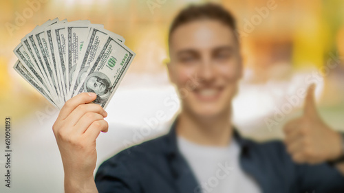 Glad millennial caucasian man in casual, show many dollars cash, thumb up gesture, win in city