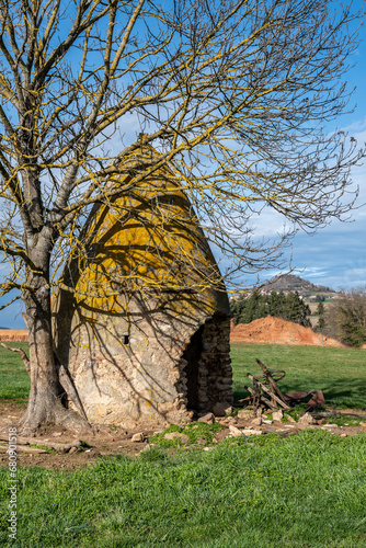 petite maison de berger en pierre avec un arbre lui faisant de l'ombre e en arrière plan le petit village d'Usson dans le puy de dôme photo